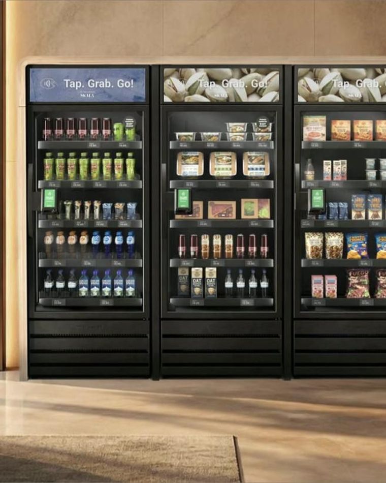 A Skala AI smart cooler bank in a corporate lobby, header screens reading Tap. Grab. Go.
