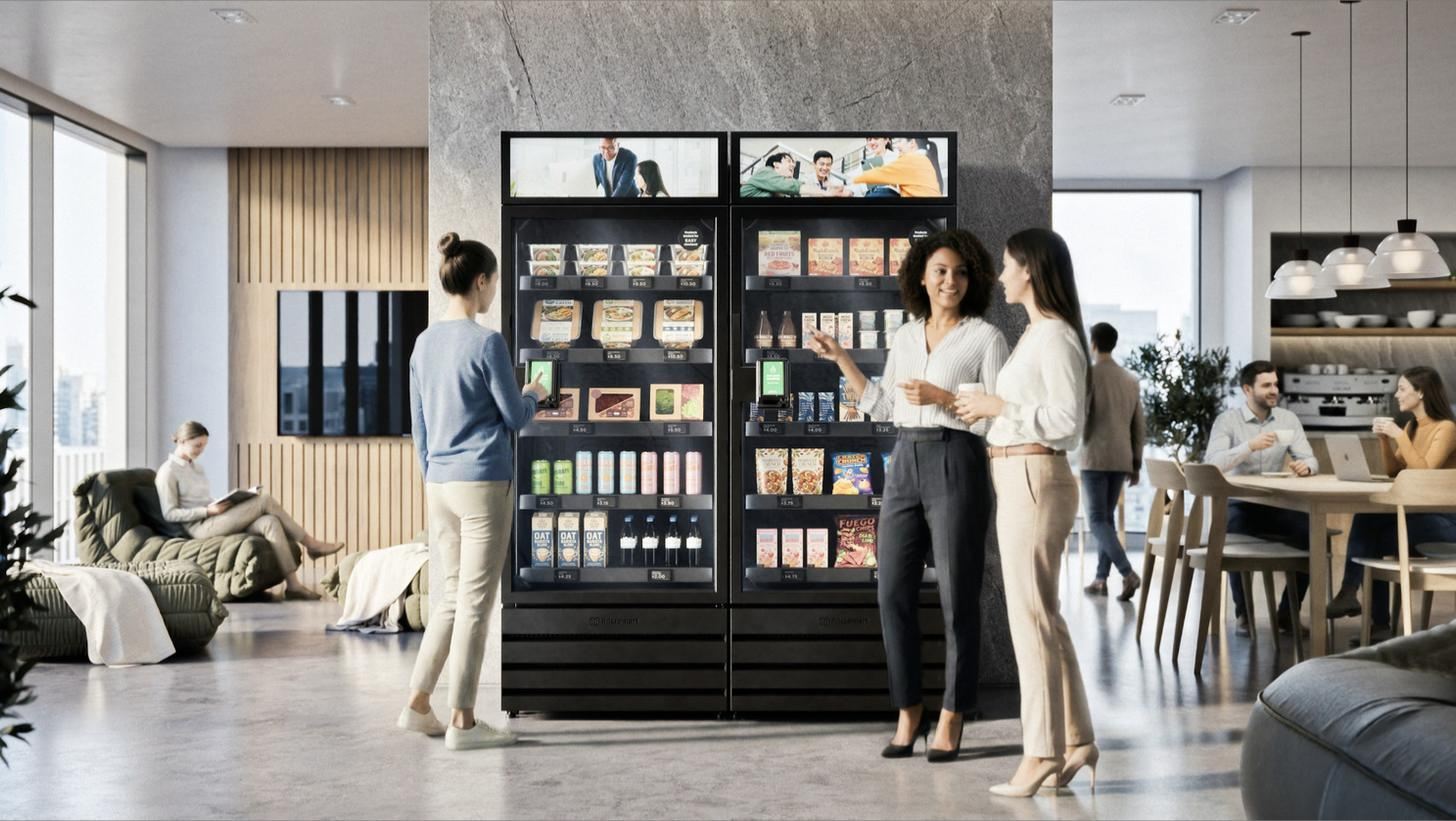 Colleagues in an office break room beside two stocked Skala AI smart coolers with digital header screens.